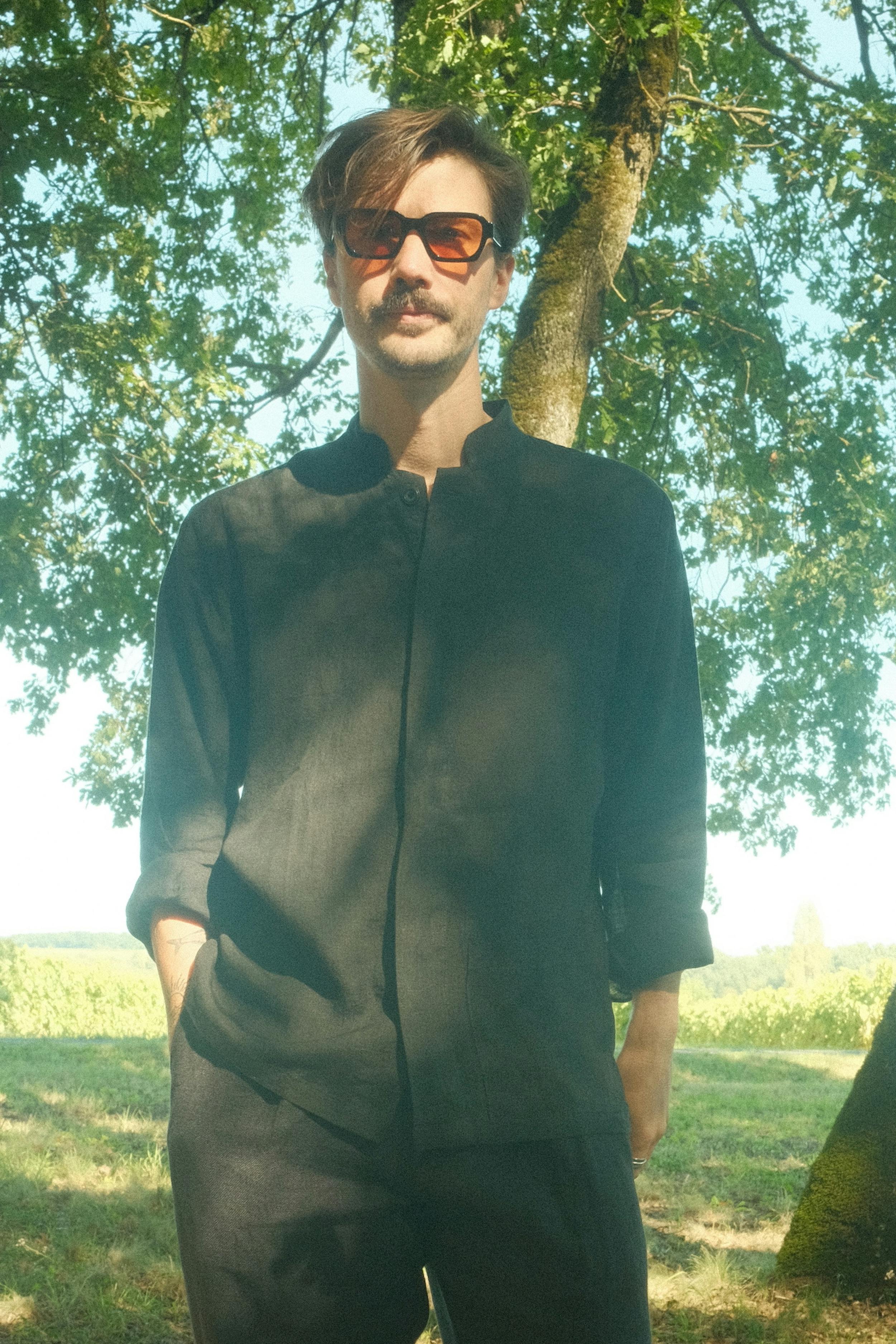 homme en chemise, pantalon et chaussures noires dans sous-bois